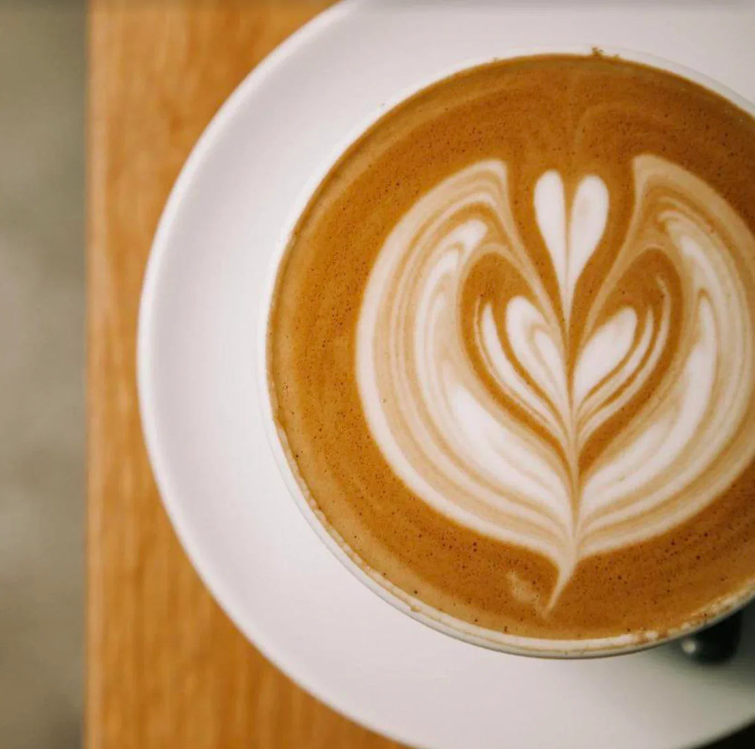 A beautifully crafted latte topped with latte art, served on a white plate, showcasing the rich color of VANILLA SYRUP.