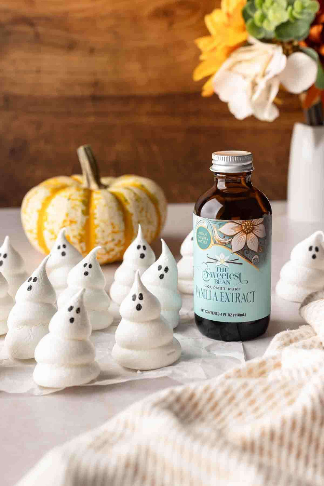 Vanilla Meringue Ghosts displayed with a bottle of vanilla extract and decorative autumn elements.